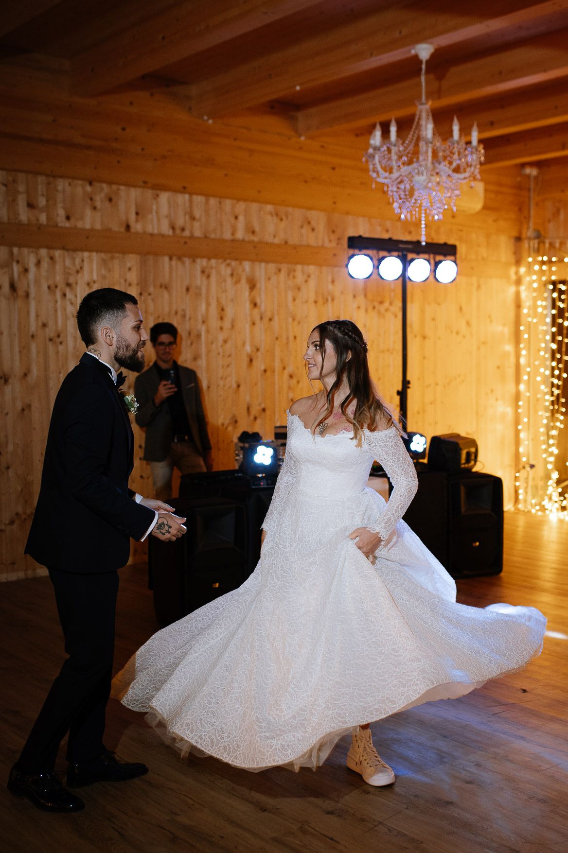A wedding couple dancing in a rustic wooden venue with twinkling lights and chandeliers.