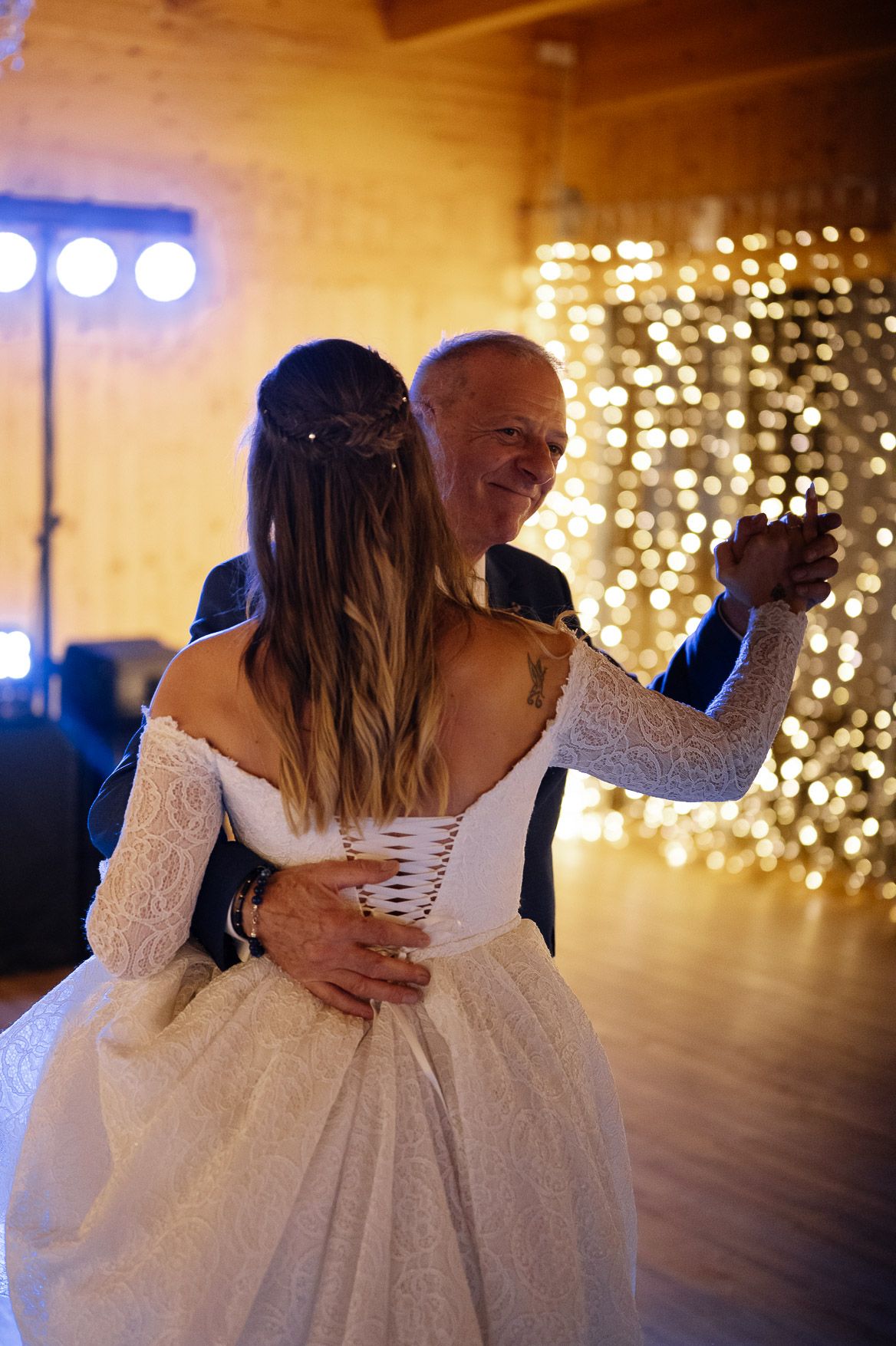 Intimate dance moment captured on wooden dance floor with string light backdrop.