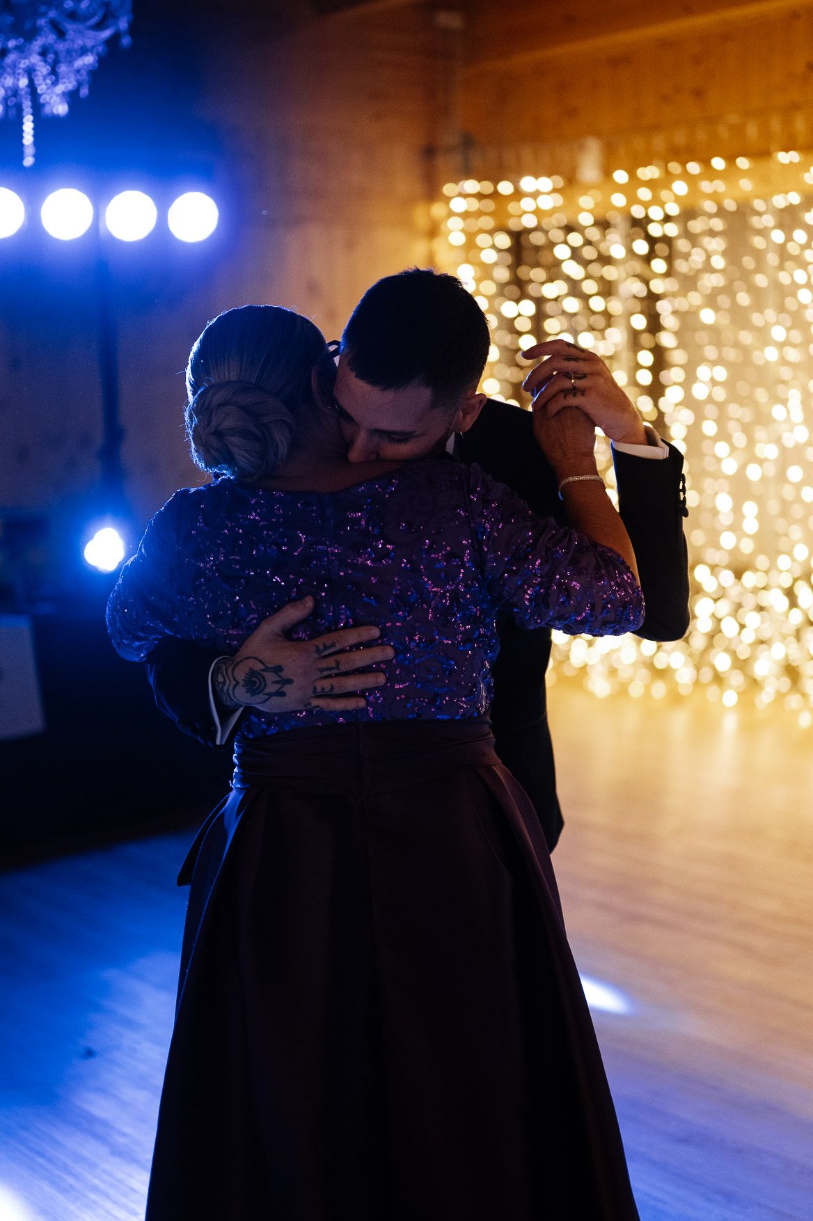 Couple sharing an intimate dance under dramatic blue lighting and sparkling backdrop.