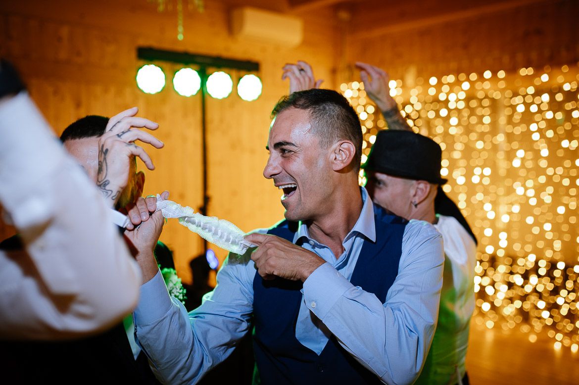 Guests celebrate with energetic dancing at a wedding reception with twinkling lights in the background.
