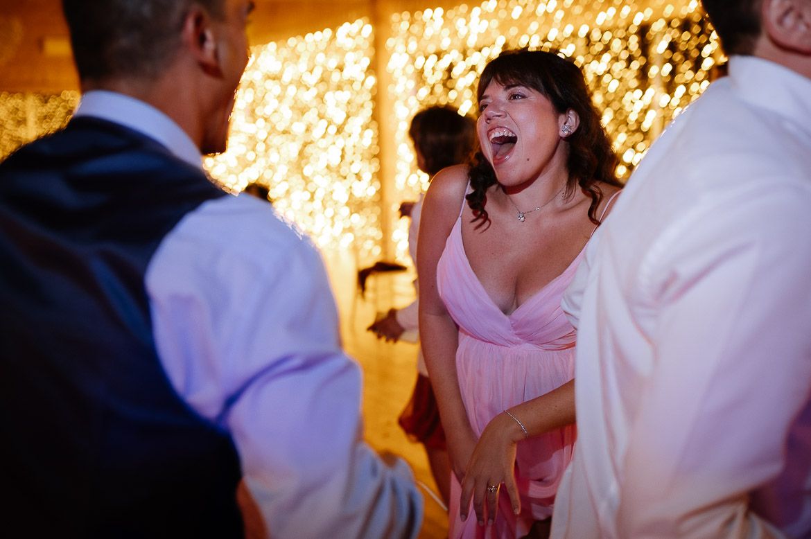 Wedding guests dancing and laughing together at a reception with warm lighting and festive atmosphere.