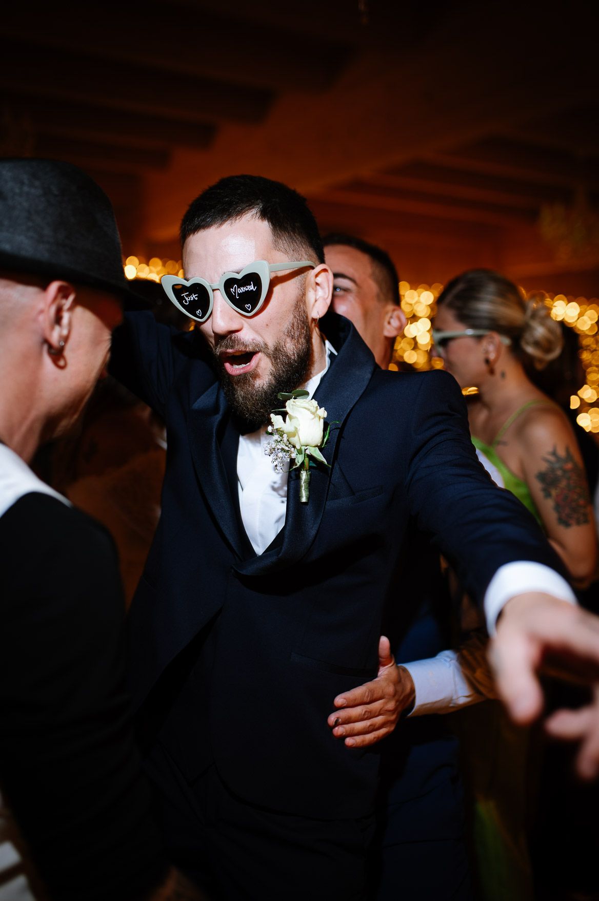 Wedding guests dance and celebrate on a dimly lit dance floor with warm ambient lighting.