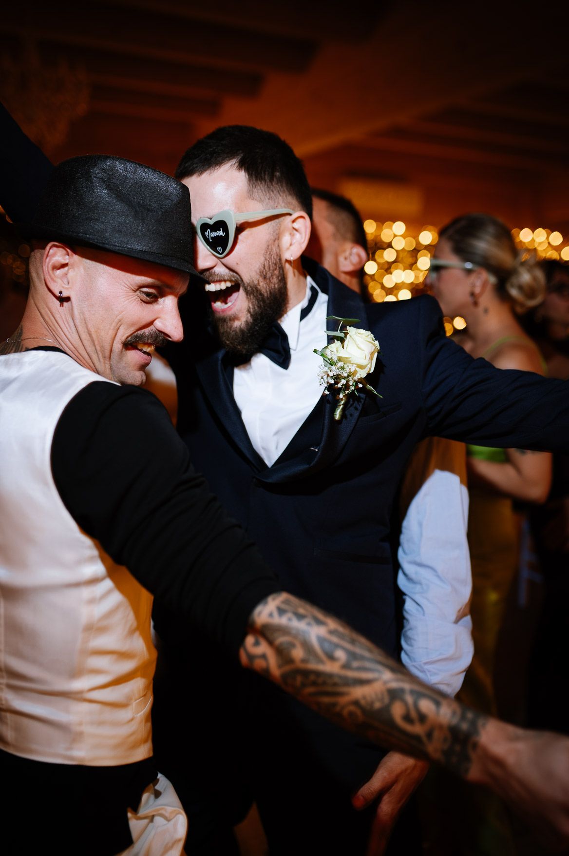 Guests in formal attire dance energetically at a wedding reception under warm lighting.