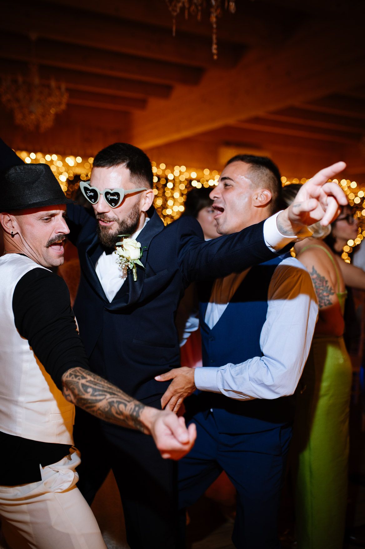 Energetic dance party scene with guests in suits and formal wear enjoying themselves on a dimly lit dance floor.