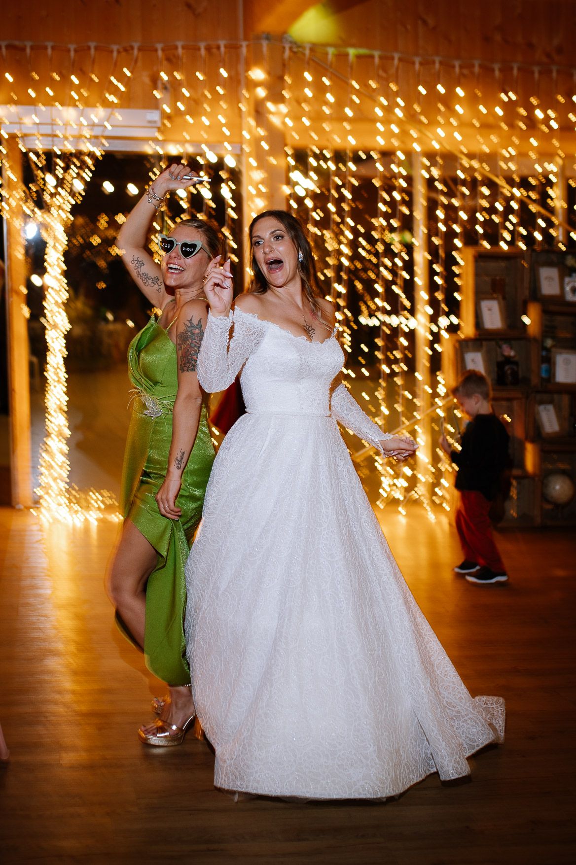 Wedding guests dancing and celebrating on a wooden dance floor under string lights.
