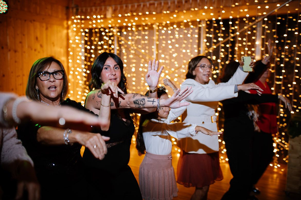 Wedding party guests dancing and celebrating under warm twinkle lights at an indoor reception.