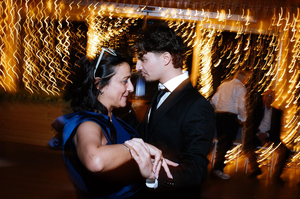 A couple shares a romantic dance moment under twinkling lights at an evening celebration.