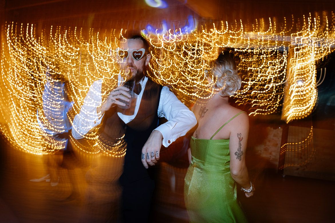 Dancing couple in formal attire twirls on dance floor with golden bokeh lights creating a magical backdrop.
