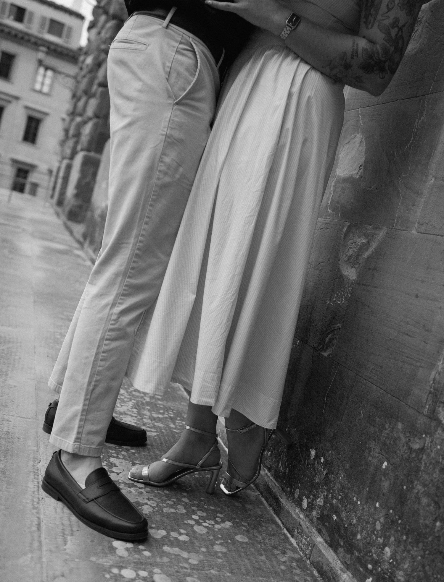 A black and white photograph showing multiple pairs of legs and white skirts standing against a wall.