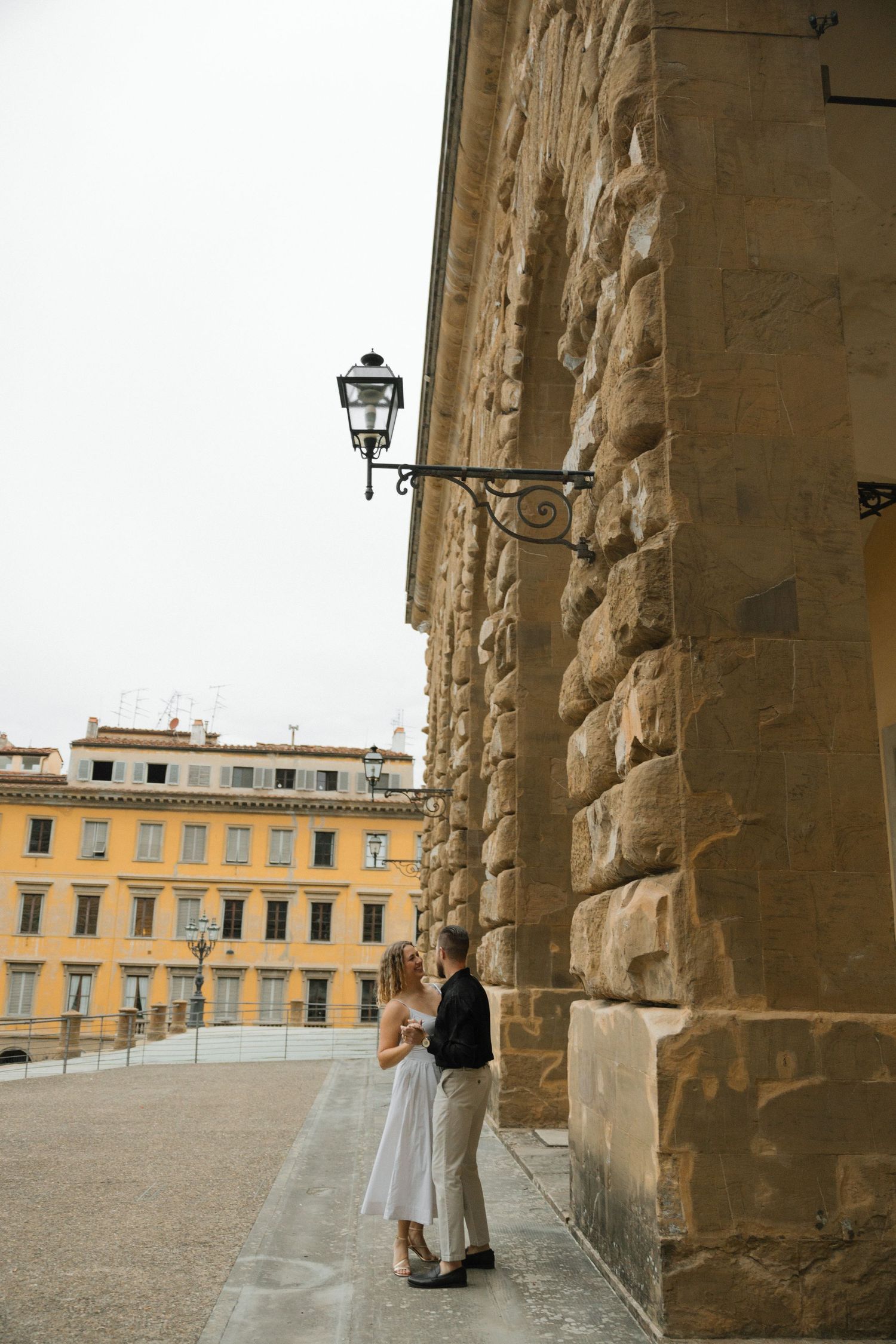 Intimate moment photographed beneath ancient stone archways with yellow buildings in view.