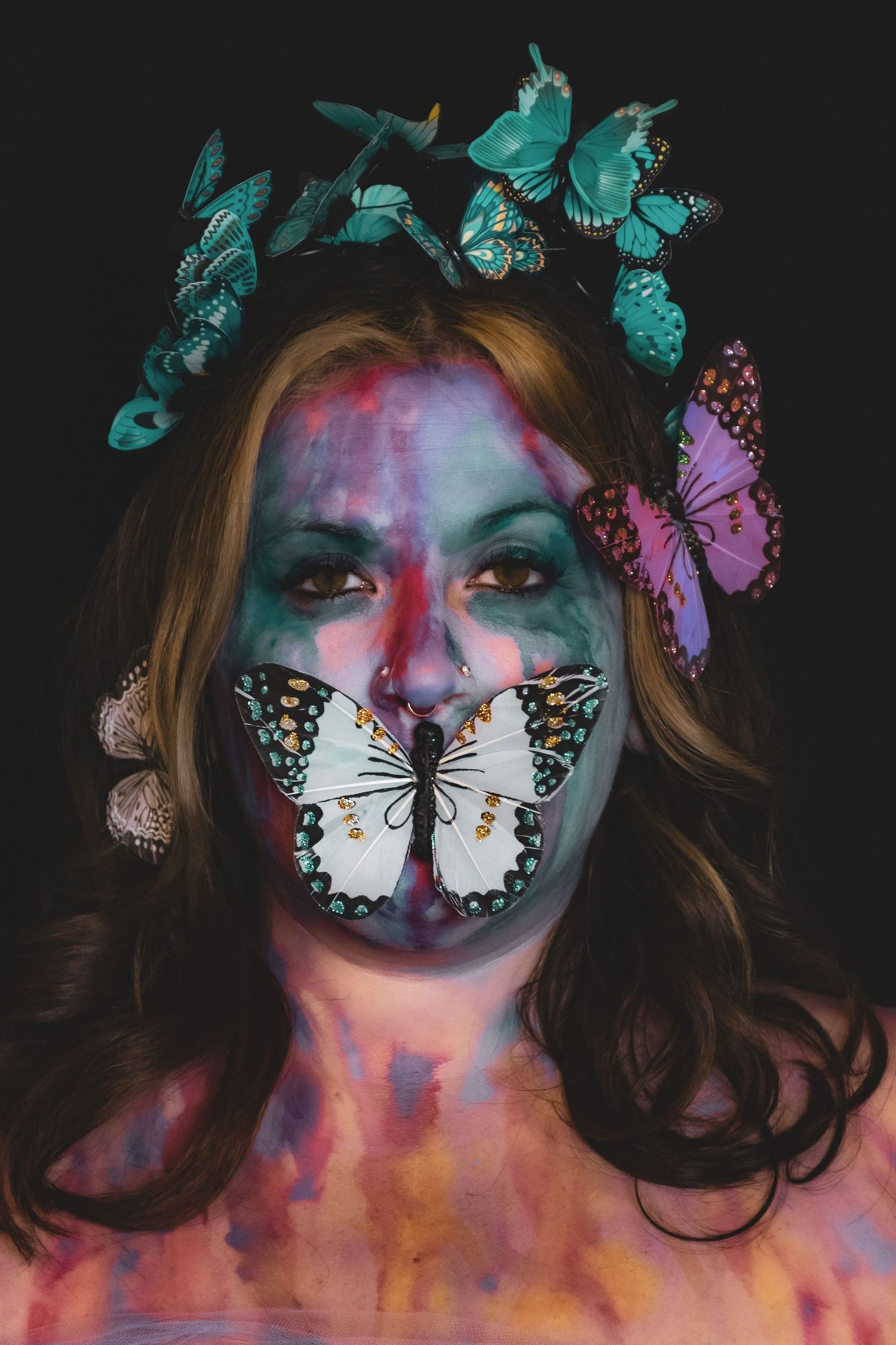 Woman with butterfly face paint and teal butterfly crown on dark background.