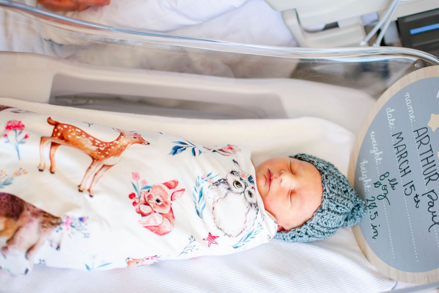 A person wearing a knit sweater holds a tiny baby swaddled in white blankets while resting on a bed.