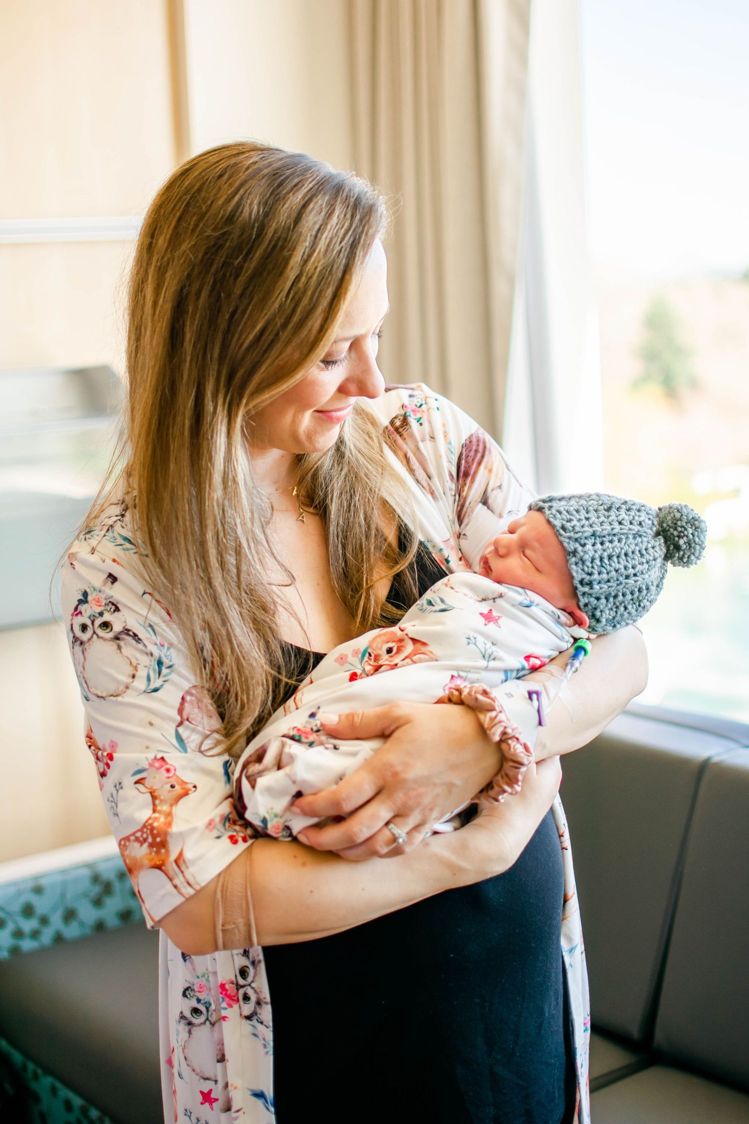 A tender moment showing a parent in floral dress cradling and bonding with a newborn baby in a bright living room.