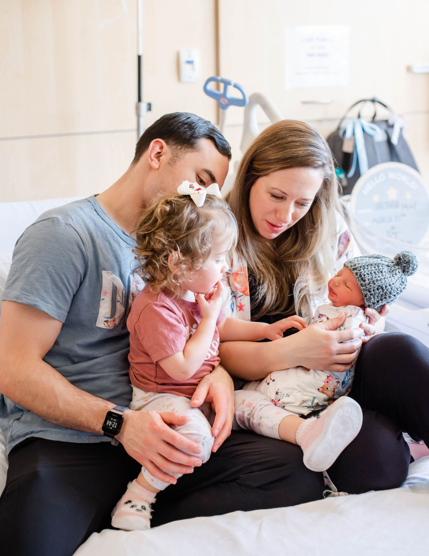A tender moment with a newborn baby wearing a knitted hat being cradled and admired by loved ones.