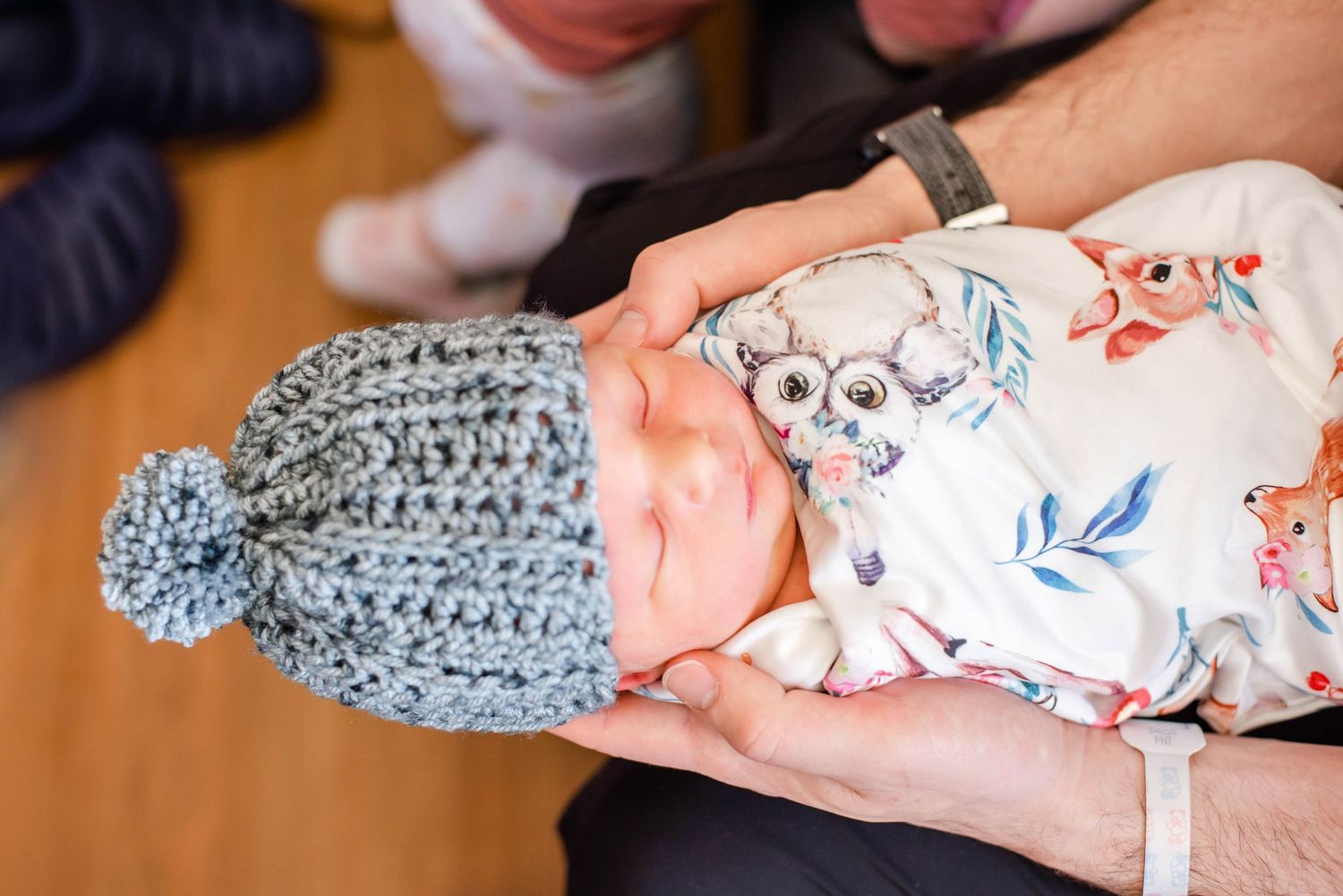 Close-up shots of a sleeping newborn wearing a blue knit hat being held by caring hands.