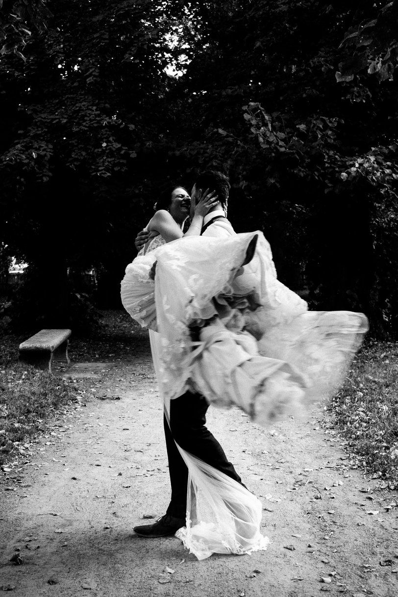 A dramatic black and white wedding photo of a couple twirling on a forest path with the bride's dress flowing.