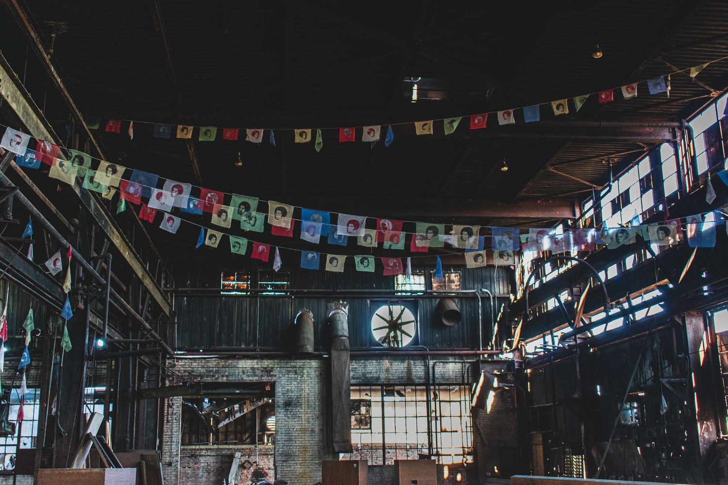 Industrial venue interior with colorful hanging prayer flags and vintage clock.