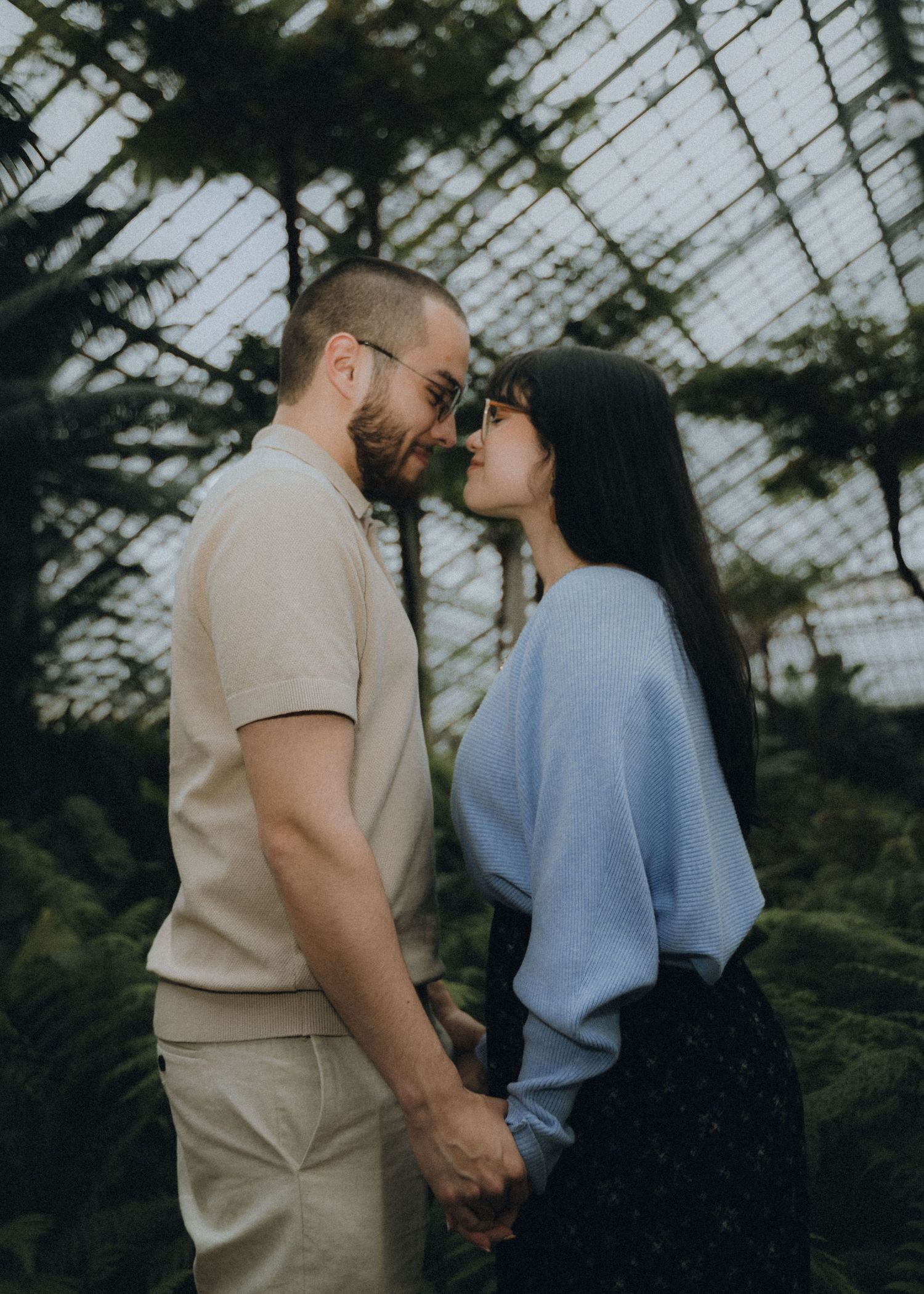A couple embraces in a romantic moment by a lake with trees in the background on an overcast day.