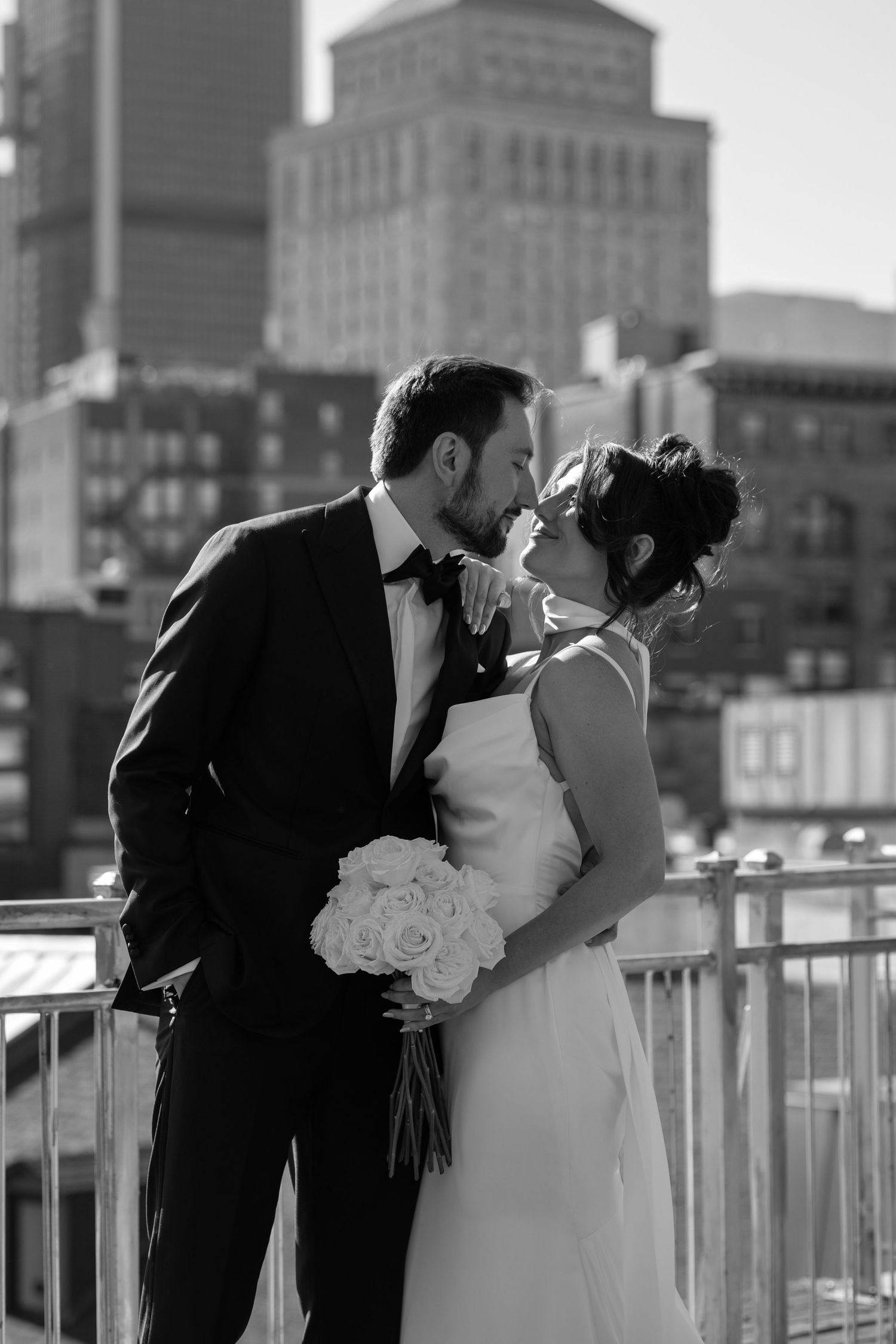 A romantic black and white photo series of a couple sharing a kiss on a city rooftop with buildings in the background.
