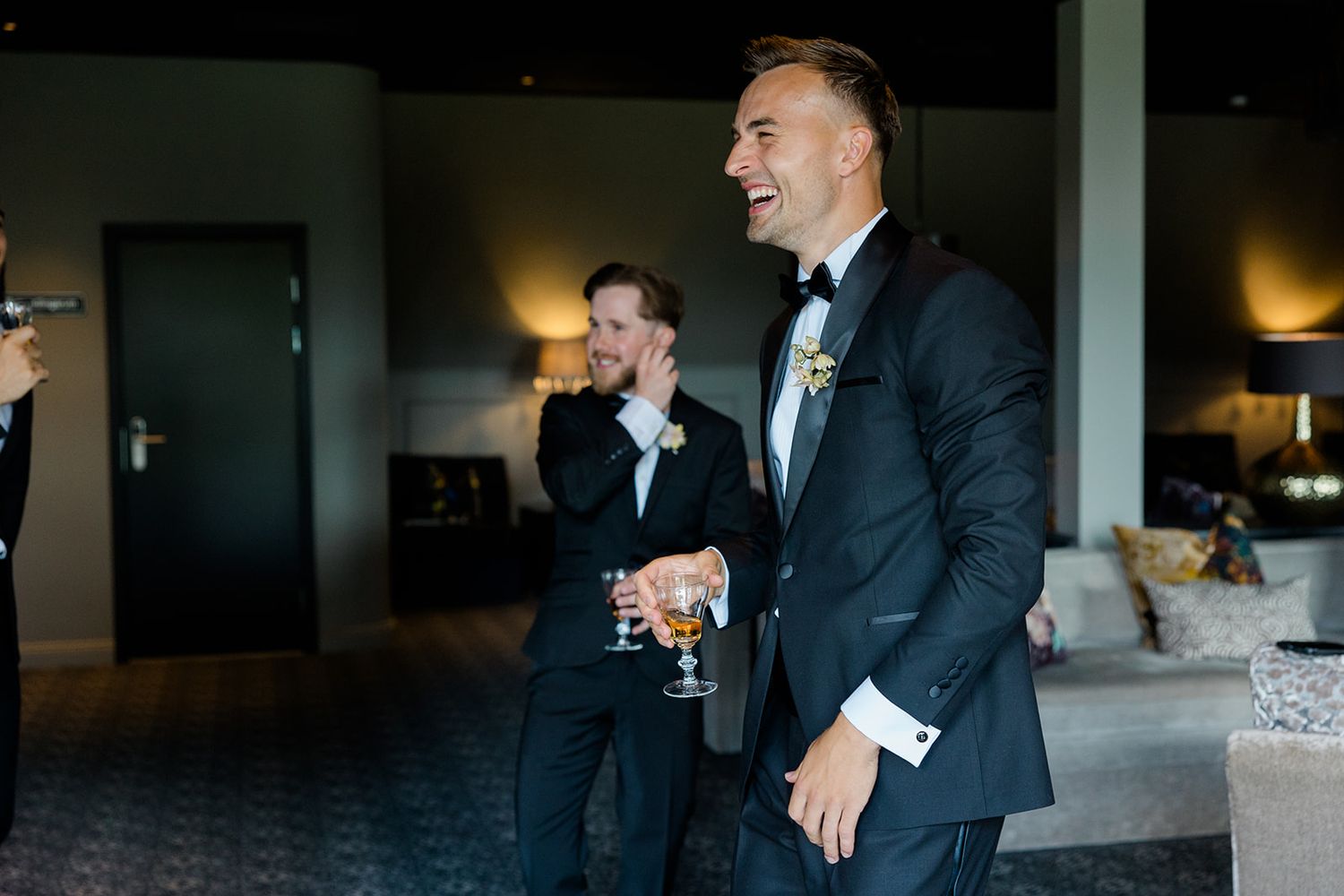 A group of people in formal attire laugh and share a candid moment at an elegant indoor event.