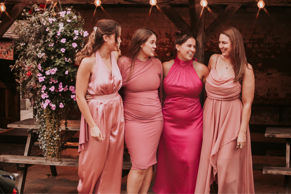 Bridesmaids in pink and coral dresses pose together at wedding celebration.