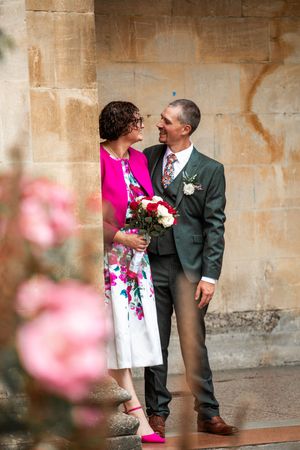 A couple poses against a stone wall, with the person wearing a vibrant pink dress and white pattern.
