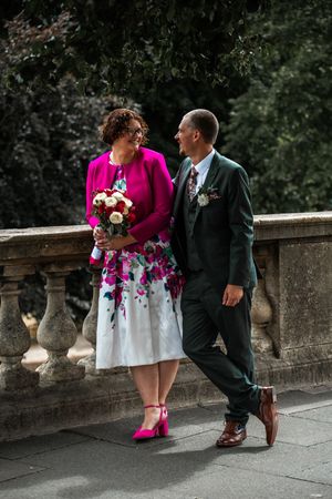 A couple in formal attire poses on stone steps, with bright pink shoes adding a pop of color.Bath Guildhall Wedding