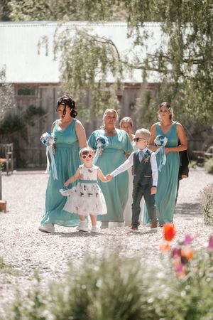 Wedding party in turquoise dresses walks together on a sunny day through a garden setting. Hayne, Devon