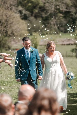 Wedding guests shower the happy couple with white confetti petals during an outdoor ceremony. Hayne, Devon