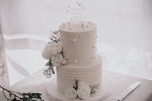 Elegant two-tier white wedding cake decorated with delicate roses and baby's breath on white tablecloth.
