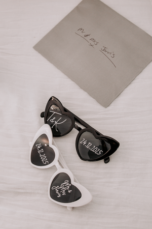 Heart-shaped sunglasses in black and white with wedding-related text displayed against a light background.