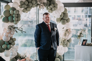 A wedding celebration decorated with elegant sage green and white balloon arches and floral arrangements in an indoor venue.