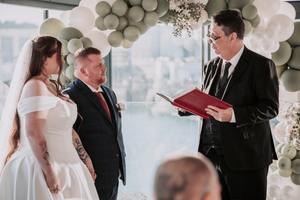 A wedding ceremony takes place under an elegant balloon arch with white and silver decorations.