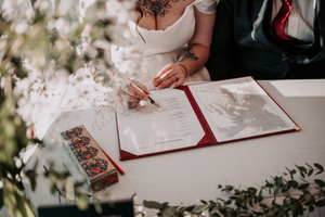 Hands signing a wedding registry or guestbook with an elegant pen on a white table at a formal event.