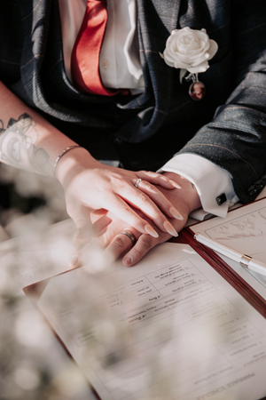 Close-up view of hands signing wedding documents with a red ribbon and white rose decoration.