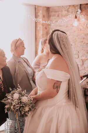 Wedding ceremony scene with soft lighting showing white dresses and floral decorations in a rustic brick venue.