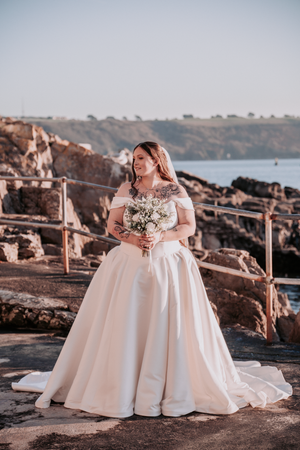 An elegant white ballgown wedding dress photographed against rocky coastal scenery at sunset.