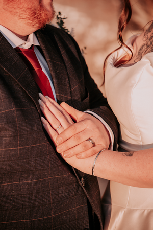 Close-up detail of wedding rings and hands against formal attire during an intimate moment.