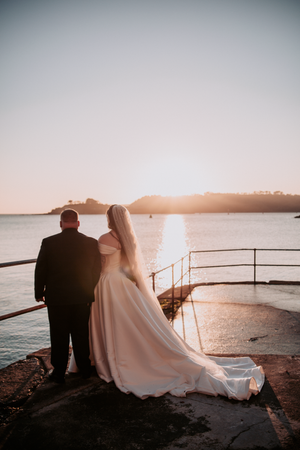 A romantic sunset wedding photo showing a couple sitting together on coastal rocks overlooking the ocean.