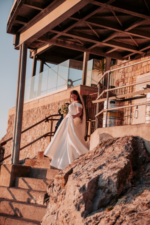 A series of wedding photos showing a bride in a flowing white dress posing against a rustic stone wall at sunset.