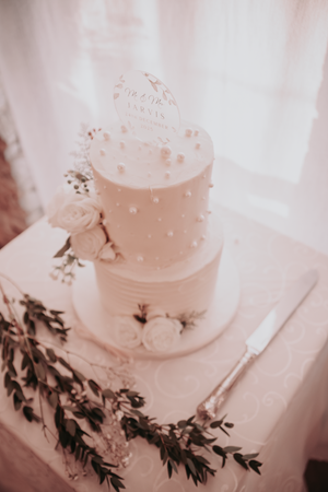 Elegant white wedding cake decorated with delicate floral details and greenery accents.