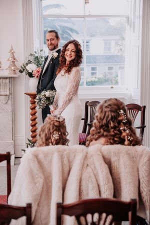 Elegant winter wedding scene with couple standing by window and bridesmaids in matching curled hairstyles and fur wraps.