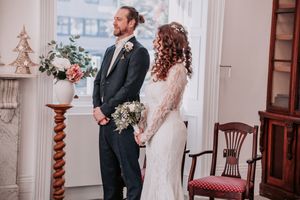 Bride and groom share a tender moment during their winter wedding ceremony in an elegant white room.