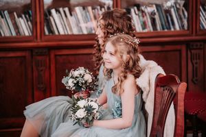 A bride in a white gown holds a bouquet while posing in a vintage library setting with dark wood shelving.