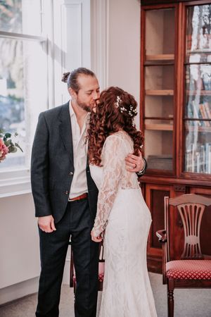 A romantic wedding couple shares intimate moments in an elegant indoor venue with vintage wooden furniture.