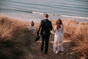 A couple walks along a scenic beach path through golden beach grass at sunset.