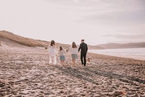 A family walks together along a sandy beach at sunset with mountains in the background.