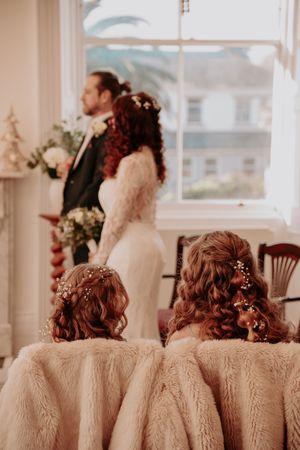 Bridesmaids in matching dresses sit together at a wedding venue with elegant decor and natural lighting.
