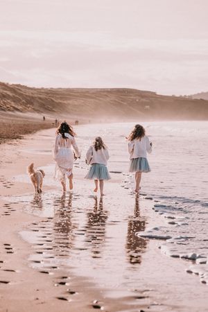 Four people walking along a beach shoreline with waves reflecting in the wet sand at sunset.