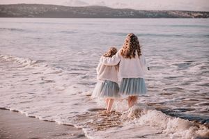 Family walking together along a scenic beach shoreline at sunset with mountains in the background.